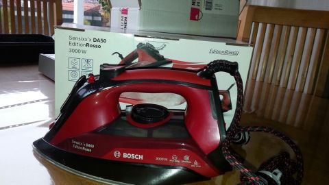 Ein rotes Bügeleisen von Bosch steht auf einem Tisch, während Verpackung im Hintergrund sichtbar ist.