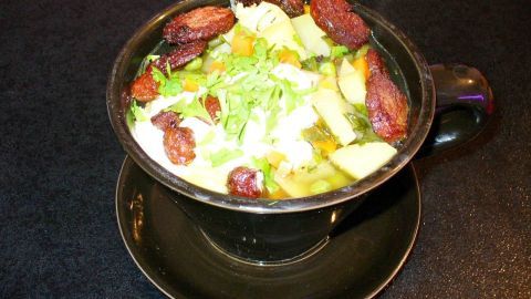 Eine schüssel Kartoffelsuppe mit buntem Gemüse und Knoblauchwurst ist dekorativ angerichtet und steht auf einem schwarzen Untergrund.