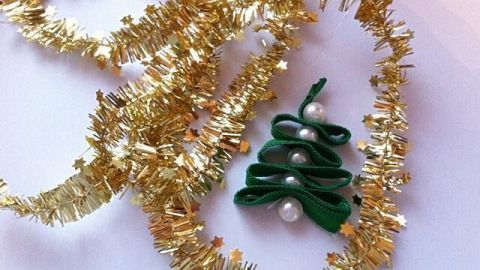 Ein grüner Weihnachtsbaum-Anhänger liegt zwischen goldenem Lametta und verleiht der festlichen Dekoration einen eleganten Akzent.