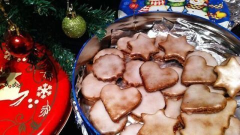 In einer bunten Dose liegen verschiedene Gewürzplätzchen in Form von Herzen und Sternen, umgeben von festlicher Dekoration.