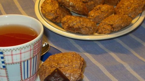 Ein Teller mit Schokoladenmakronen steht auf einem Tisch, neben einer Tasse Tee, auf einem gestreiften Tischdecken.