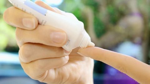 Eine Hand trägt Hirschtalgcreme aus einer Tube auf einen Finger auf, im Hintergrund unscharf grüne Natur.