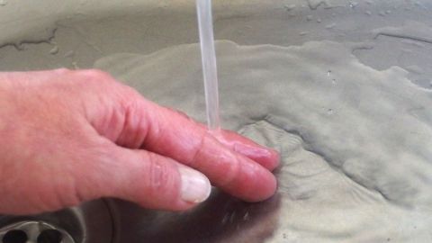 Knoblauchgeruch an den Händen kann lästig sein. In dem Artikel erfährst Du, wie du mit Edelstahl und Wasser effektiv dagegen angehst. Hier siehst du, wie du deine Hände unter fließendem Wasser reinigen kannst. Eine Hand hält unter fließendem Wasser, um Knoblauchgeruch von den Händen mit Edelstahl zu entfernen.