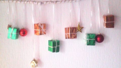 Geschenkboxen und Dekorationen hängen an einem Weihnachtszweig an der Wand, festlich arrangiert im Wohnraum.