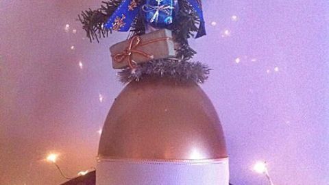 Eine goldene Deko-Weihnachtsglocke hängt dekoriert mit Tannenzweigen und Glitzer, umgeben von Lichtern und festlicher Stimmung.