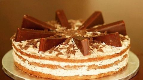 Eine schokoladige Pingui-Torte mit mehreren Schichten, dekoriert mit Schokoladenstücken, steht auf einem Tisch.