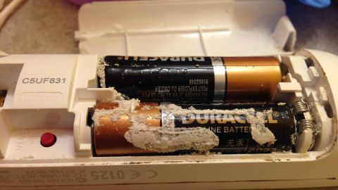 Eine geöffnete Fernbedienung mit ausgelaufenen Batterien, die gereinigt werden müssen, liegt auf einer Arbeitsfläche.