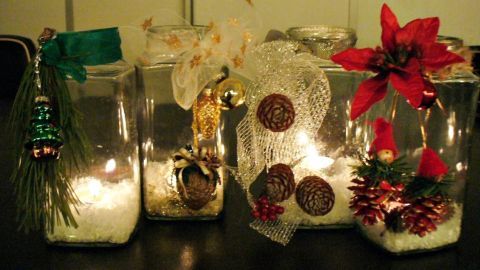 Weihnachtlich geschmückte Windlichter leuchten sanft auf einem Tisch und sind mit festlichem Dekor und Pflanzen verziert.