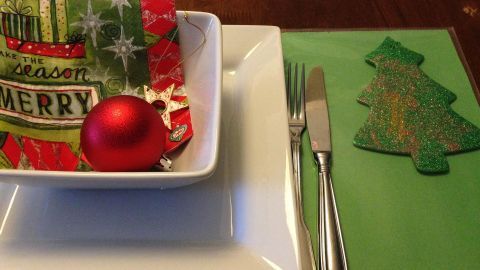 Ein grünes Platzdeckchen liegt auf dem Tisch, dekoriert mit einer roten Weihnachtskugel und einer festlichen Serviette.