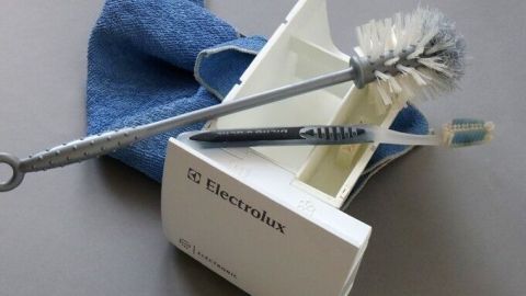 Eine Bürste und ein Tuch liegen auf einem Tisch, während die Waschmaschine gereinigt wird, um muffigen Geruch zu beseitigen.