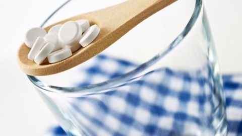 Holzlöffel mit weißen Tabletten liegt auf einem Glas, das auf blau-weiß kariertem Tuch steht.