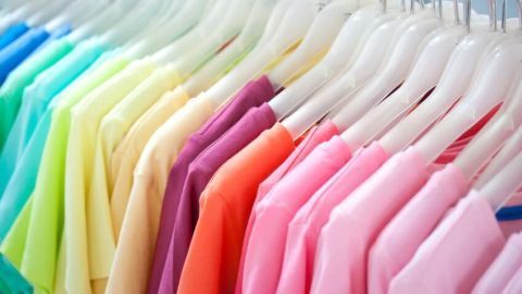 Bunte T-Shirts hängen ordentlich auf weißen Kleiderbügeln in einer Reihe in einem Kleiderschrank oder Geschäft.