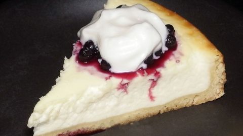 Ein Stück kalorienarmer Käsekuchen liegt auf einem Teller, garniert mit schwarzer Schlagsahne und Fruchtsoße.