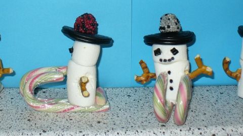 Marshmallow Schneemänner stehen mit verschiedenen Hüten auf einer Fläche, umgeben von einer blauen Wand.