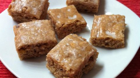 Walnuss-Schnitten liegen auf einem weißen Teller auf rotem Tischläufer. Sie sind quadratisch und mit Zuckerguss überzogen.