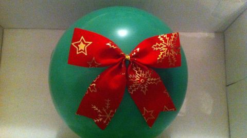Ein grüner Luftballon mit rotem Satinband und Weihnachtsmotiven liegt in einer offenen Geschenkbox.