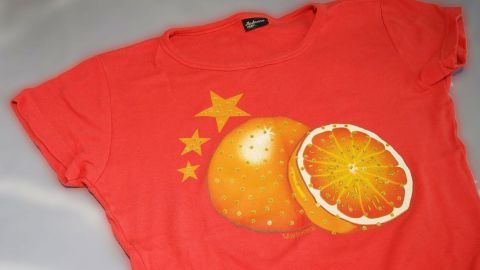 Ein rotes T-Shirt mit einem bunten Orangendesign liegt auf einem hellen Hintergrund, bereit zum Falten oder Waschen.