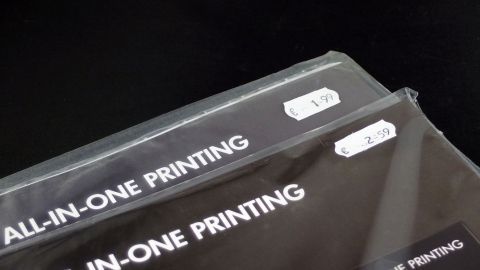 Zwei Verpackungen für All-in-One-Druckprodukte liegen auf einem schwarzen Hintergrund, die Preise sind sichtbar angebracht.