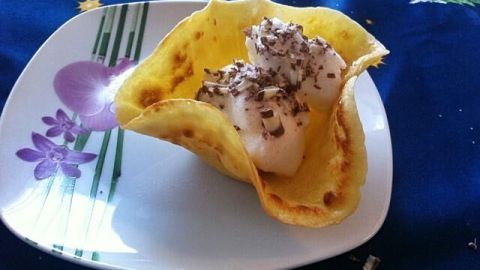 Eine gefaltete Pfannkuchen-Schale hält eine Portion Eiscreme, dekoriert mit Schokolade, auf einem blühenden Teller.
