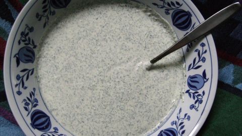 In einem bunten Tuch liegt eine Schale mit Grüne Sauce, verziert mit Blumenmotiven, in die ein Löffel steckt.