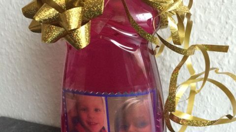 Eine Spülmittelflasche mit einem goldenen Geschenkband und Bildern auf der Vorderseite steht auf einer dunklen Oberfläche.