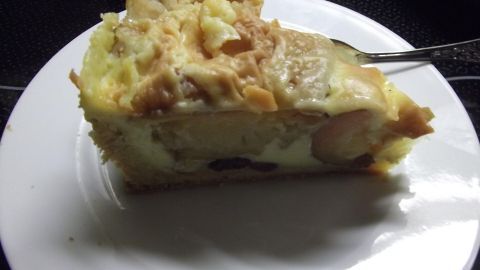Ein Stück Bratapfelkuchen liegt auf einem weißen Teller, mit einer Gabel daneben, in einem dunklen Raum.
