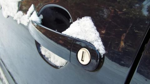 Ein schwarzes Auto mit einem eingefrorenen Türschloss, umgeben von Schnee, ist bereit zum Öffnen.