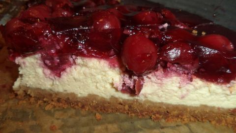 Ein cremiger Käsekuchen ist in Stücke geschnitten und mit einer glänzenden Kirschdecke verziert, auf einem rustikalen Tisch.