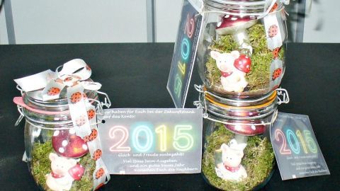 Glasgefäße mit Moos und kleinen Figuren, Geschenk zu Neujahr. Etikett zeigt „2015“, dekorative Bänder mit Marienkäfern.