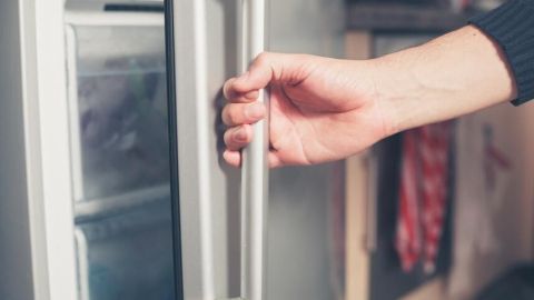 Eine Hand öffnet einen Gefrierschrank in einer Küche, um Eisschichten zu kontrollieren.
