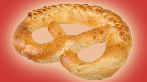 Eine große, goldbraune Neujahrsbrezel liegt auf einem roten Hintergrund und wirkt einladend und festlich.