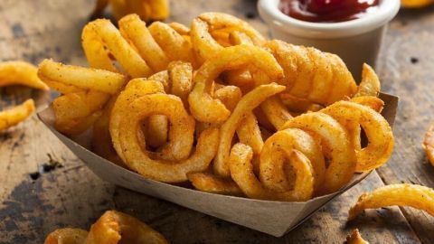 Knusprige Curly Fries in einer Pappschale auf Holztisch, serviert neben einer weißen Schale mit Ketchup.