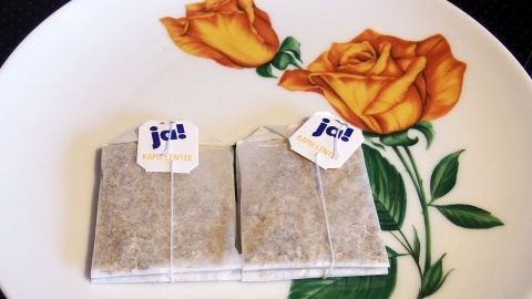 Zwei Teebeutel liegen auf einem blumenverzierten Teller, bereit, in heißes Wasser gegeben zu werden.