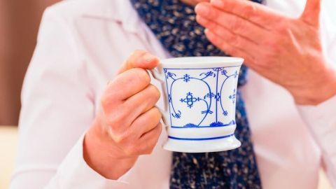 Eine Person hält eine Tasse mit blauer Verzierung, während sie sich an den Hals fasst, um gegen trockenen Reizhusten zu reagieren.