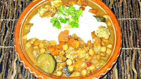 Eine Schüssel Süßkartoffelsuppe ist gefüllt mit buntem Gemüse und Garnierung aus frischem Koriander, auf einem leinen Tisch.