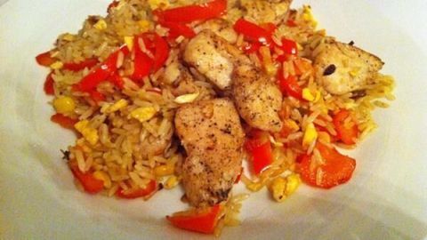 Auf einem weißen Teller liegt gebratener Reis mit saftigen Hühnerbrustfiletstücken und frischen Tomaten.