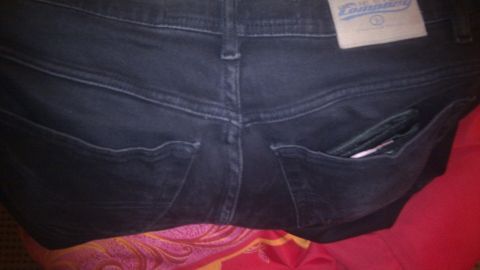 Dunkle Jeans liegen auf einem rot-gelben Stoff, die Rückentaschen sind sichtbar und scheinen einige Gegenstände zu enthalten.