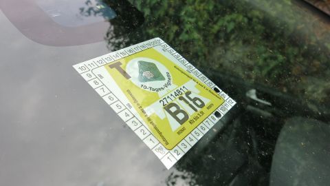 Auf der Windschutzscheibe eines Autos liegt eine gelbe Autobahnvignette, die entfernt werden soll. Hintergrund ist grün.