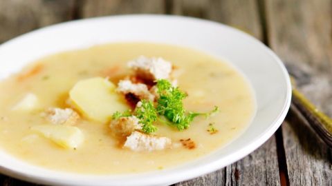 In einer weißen Schüssel liegt cremige Kartoffelsuppe, garniert mit Brotkrumen und frischer Petersilie, auf einem rustikalen Holztisch.