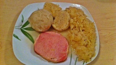 Ein Teller zeigt Kasseler, serviert mit Sauerkraut und Gwichste Knödel (Mehlknödel) in einer hellen Umgebung.