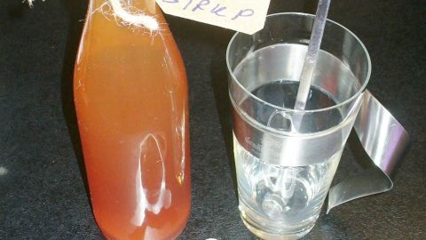 Ein Glas steht neben einer Flasche mit orientalischem Sirup und einer kleinen Kanne mit losen Teeblättern.
