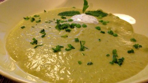 Eine cremige Erbsensuppe liegt in einer weißen Schale, garniert mit frischem Koriander und einem Klecks Minze-Zitronen-Creme.