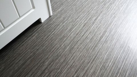 Ein grauer PVC-Boden glänzt und reflektiert Licht, während er neben einer weißen Tür verlegt ist.