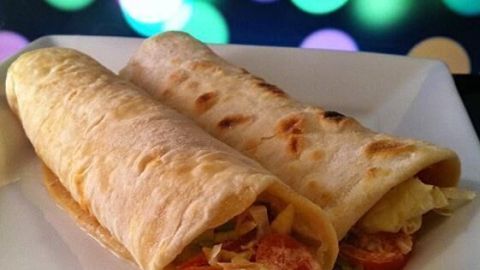 Zwei Wraps mit Thunfischfüllung liegen auf einem weißen Teller, umgeben von verschwommenen, bunten Lichtern.