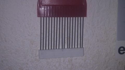 Ein roter Zwiebel-Schneider hängt an einer hellen Wand, bereit, Zwiebeln ohne Tränen zu schneiden.