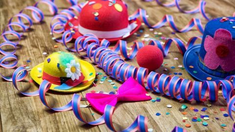 Bunte Faschingsklamotten und Konfetti liegen auf einem Holztisch, umgeben von spiralförmigen Bändern und Dekorationen.