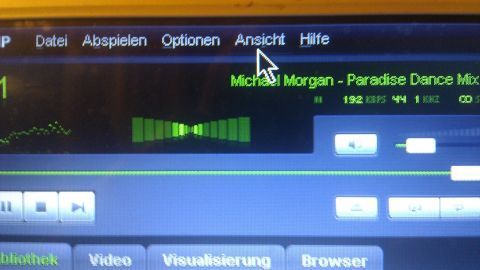 Ein Musikplayer auf dem PC zeigt eine laufende Visualisierung und spielt den Titel „Michael Morgan - Paradise Dance Mix“ ab.