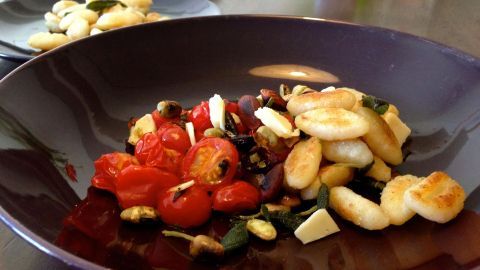 Aromatische Salbei-Gnocchi liegen zusammen mit Kirschtomaten auf einem lila Teller, umgeben von einer gemütlichen Tischatmosphäre.
