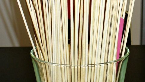 Ein Glas steht auf einem Tisch und enthält eine Mischung aus langen Holzspießen und bunten Messern, die stabilisiert sind.