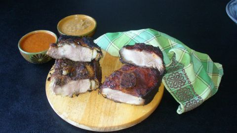 Zart gegarter Schulterbraten liegt auf einem Holzbrett, umgeben von zwei Saucen und einem gewaschenen Geschirrtuch.